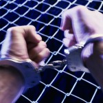 close up of mans hands in handcuffs on metal fence